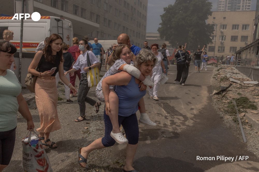 A woman carries a girl next to a damaged building of the Ohmatdyt Children's Hospital following a Russian missile attack in Kyiv