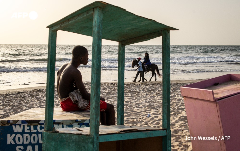 A man looks as a woman takes a horse ride along a beach