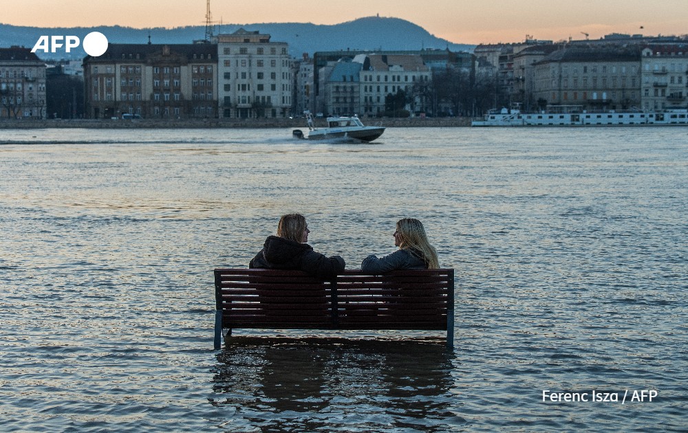 Women sit on a bench surrounded by flood water