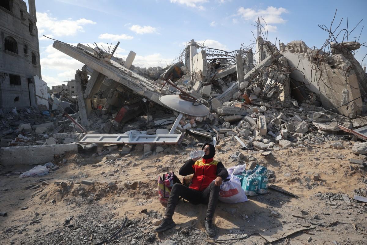 A Palestinian man drinks water as he sits next to belongings by a destroyed house in Rafah